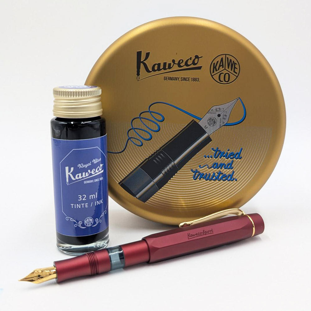 A Kaweco fountain pen in metallic burgundy with a gold nib, displayed alongside a 32 ml bottle of blue ink and a round gold metal packaging on a white background.